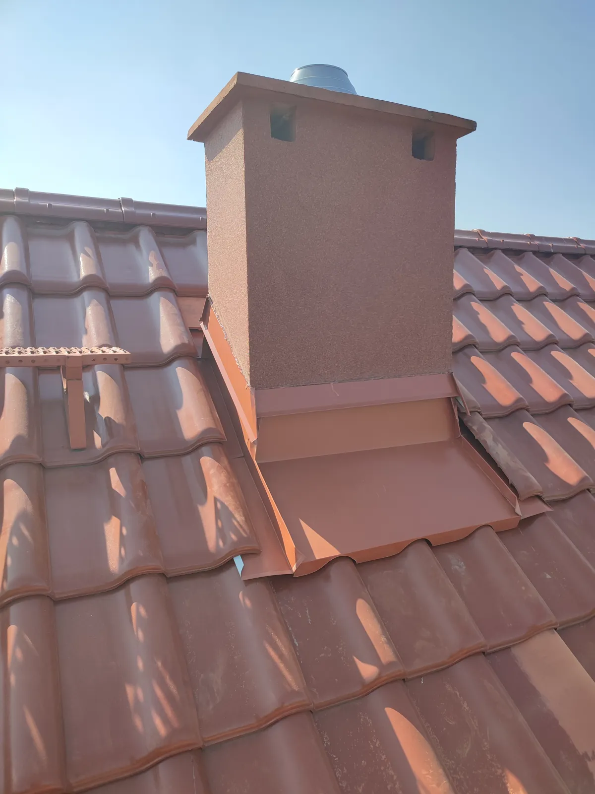 Naprawa obróbki komina w Długołęce. Obróbka zrobiona z blachy powlekanej matowej metodą na felc. Opaska jest wcięta w komin na tzw. "wydrę".